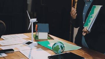 A man is standing at a table with papers and a wind turbine video