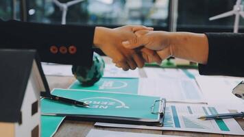 Two business people shaking hands over a table with papers and a house video