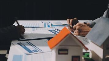 Two people sitting at a table with a house model video