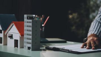 A man is writing on a paper with a pen and a house model in the background video