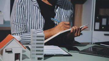 A woman writing in a notebook with a pen and a house model video