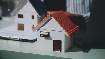 A man is working on a laptop and a house model video