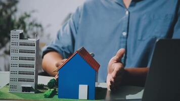 Man holding a model of a house and laptop in front of a building video