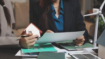 Two businesswomen are holding papers and a house model video