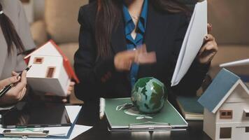 Two businesswomen are sitting at a table with a house and a globe video