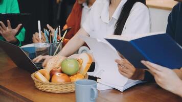 A group of people sitting at a table with laptops and books video