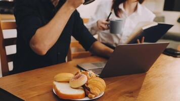 A man and woman sitting at a table with a laptop and croissants video