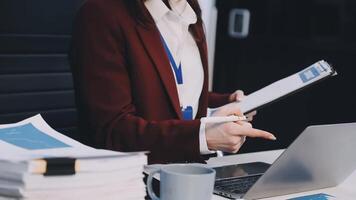 A woman in a business suit is holding a clipboard and pointing at a laptop video