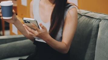 A woman holding a cup of coffee and using her phone video