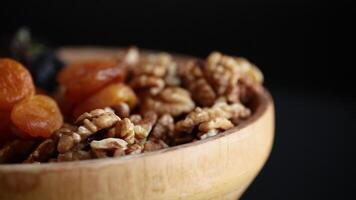 dried apricots and prunes, nuts in a wooden bowl on a dark background. video