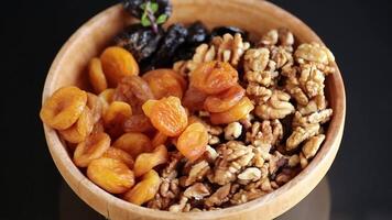 Prunes and dried apricots and nuts in a wooden bowl on a dark background. video