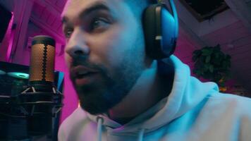 Happy Caucasian guy addict streamer male vlogger man gaming play game tournament computer vlog cyber sport gamer discussing talk microphone tech smiling blogger blogging at home neon influencer stream video