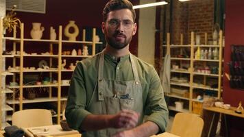Confident successful smiling Caucasian salesman seller potter male man guy businessman artist small business owner in glasses crossed arms hands looking camera smile indoor sell pottery store workshop video