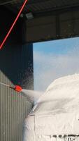 A man using a pressure washer to clean a car covered in soap foam video
