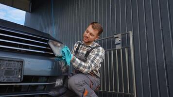 A cheerful car wash worker carefully polishes the front grill of a vehicle with a microfiber cloth video