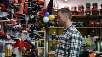 A man examines a red leaf blower displayed on a shelf in a hardware store video