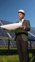 Engineer analyzing blueprints near solar panels in green field video