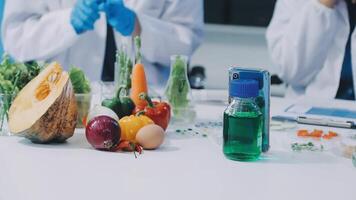 Two people in lab coats are working on a table with vegetables and other food video