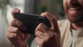 Caucasian man cyber gamer user mobile phone playing game at home gadget addicted player male guy play online gaming addiction gambling smartphone entertainment device browsing internet enjoy fun video