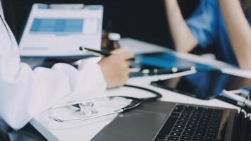 A doctor is working on a laptop while a woman sits at a desk video