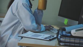 A woman in a lab coat is sitting at a desk with a cup of coffee video