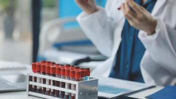 A doctor is holding a blood sample in front of a computer video