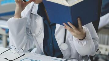 A woman in a lab coat talking on a phone while reading a book video