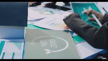 A person is sitting at a table with papers and a net zero logo video