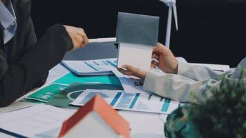 Two people sitting at a table with papers and a house video