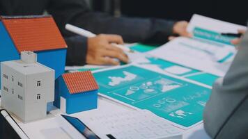 A man and woman are working on a document with a house model video
