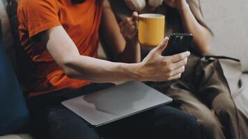A man and woman sitting on a couch with a laptop and a cup of coffee video