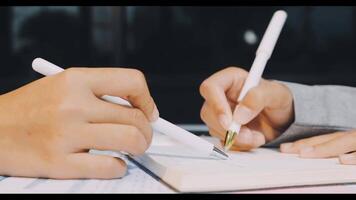 Two people writing on a notebook with a pen video