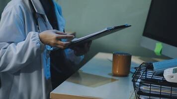 A doctor is holding a clipboard and looking at a computer screen video