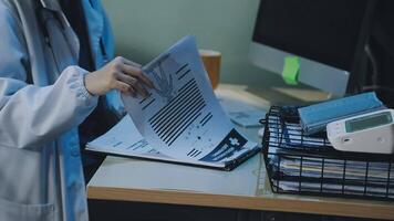 A doctor is working on paperwork in front of a computer video