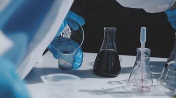 A person in a lab coat is pouring liquid into a beaker video