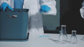 Two people in lab coats and gloves are working on a table video