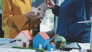 Two people holding a house model in front of a table video