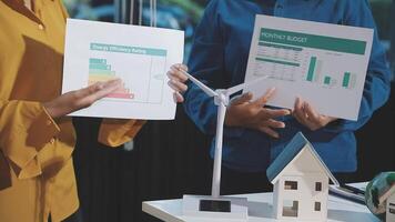 Two people holding papers with a wind turbine and house video