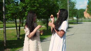 Two beautiful girlfriends with a good mood walk in the park and make soap bubbles in summer sunny weather video