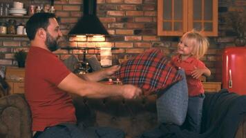 Happy father with little son sitting on the sofa fooling around and beat each other with pillows video