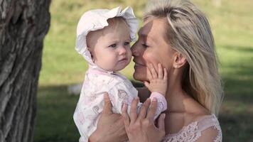Mother and little daughter hugging and playing while sitting near tree on lawn video