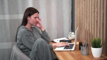 A woman has a headache and massages her temples while sitting at her desk while working from home. video