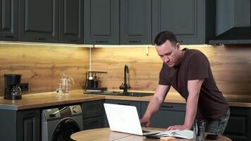 Male businessman works from home standing at the table using a laptop. End of the working day. video