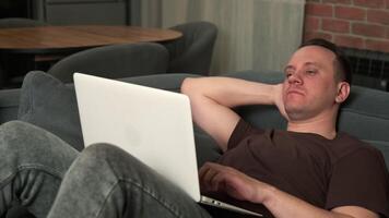 Tired man using laptop and falling asleep lying on sofa at home. video