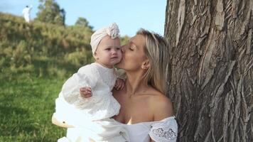Mother and little daughter hugging and playing while sitting near tree on lawn video