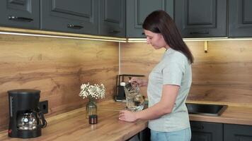 Woman drinks water from a glass while standing in the kitchen in the morning video