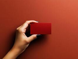Elegant hand holding a red business card against a warm brown background in subtle lighting photo