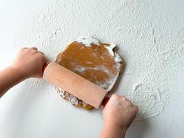 Child rolling dough on floured surface with rolling pin photo