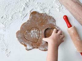 Child making heart shaped cookies with dough and rolling pin photo