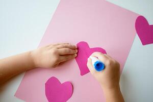 Child gluing pink paper hearts on craft project photo